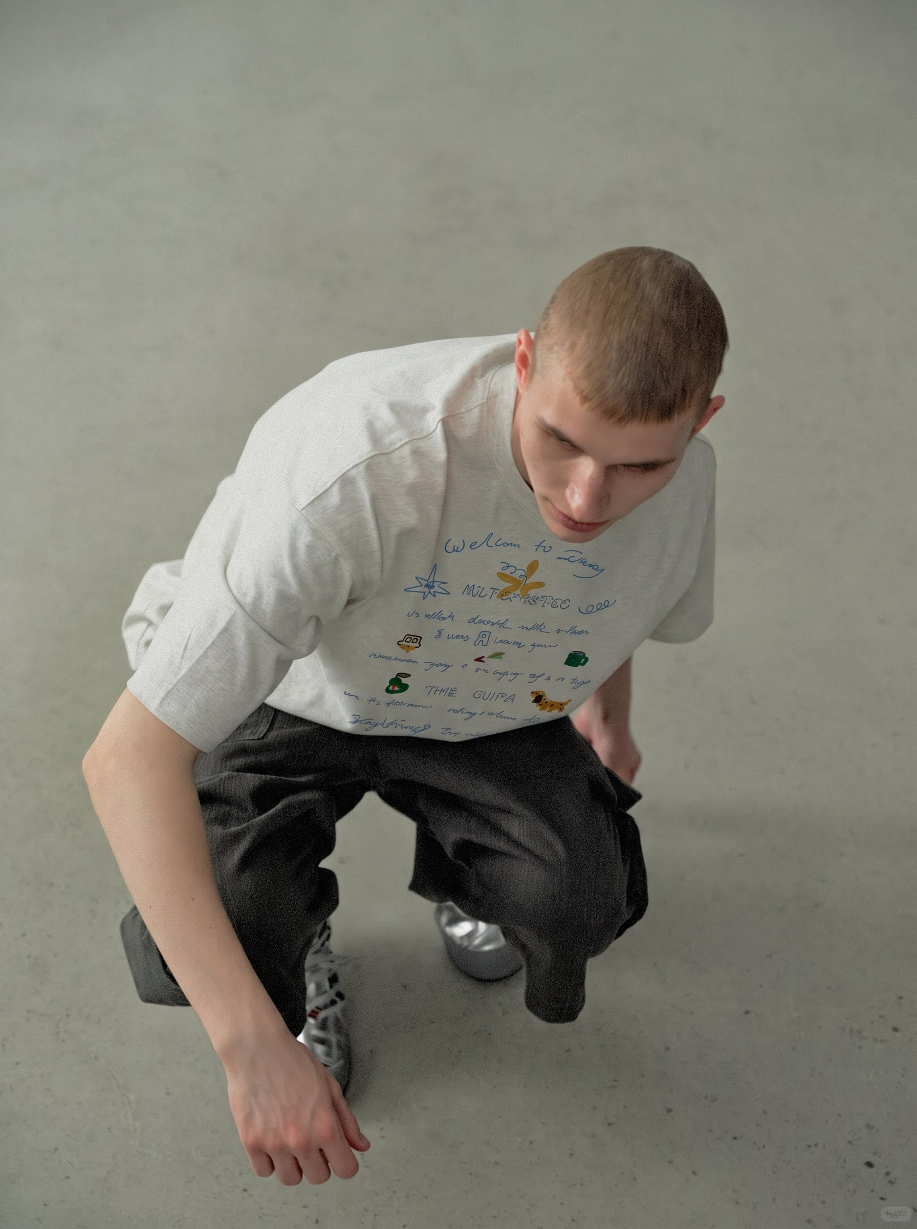 Person wearing a white t-shirt with colorful graphics and dark pants on a plain background