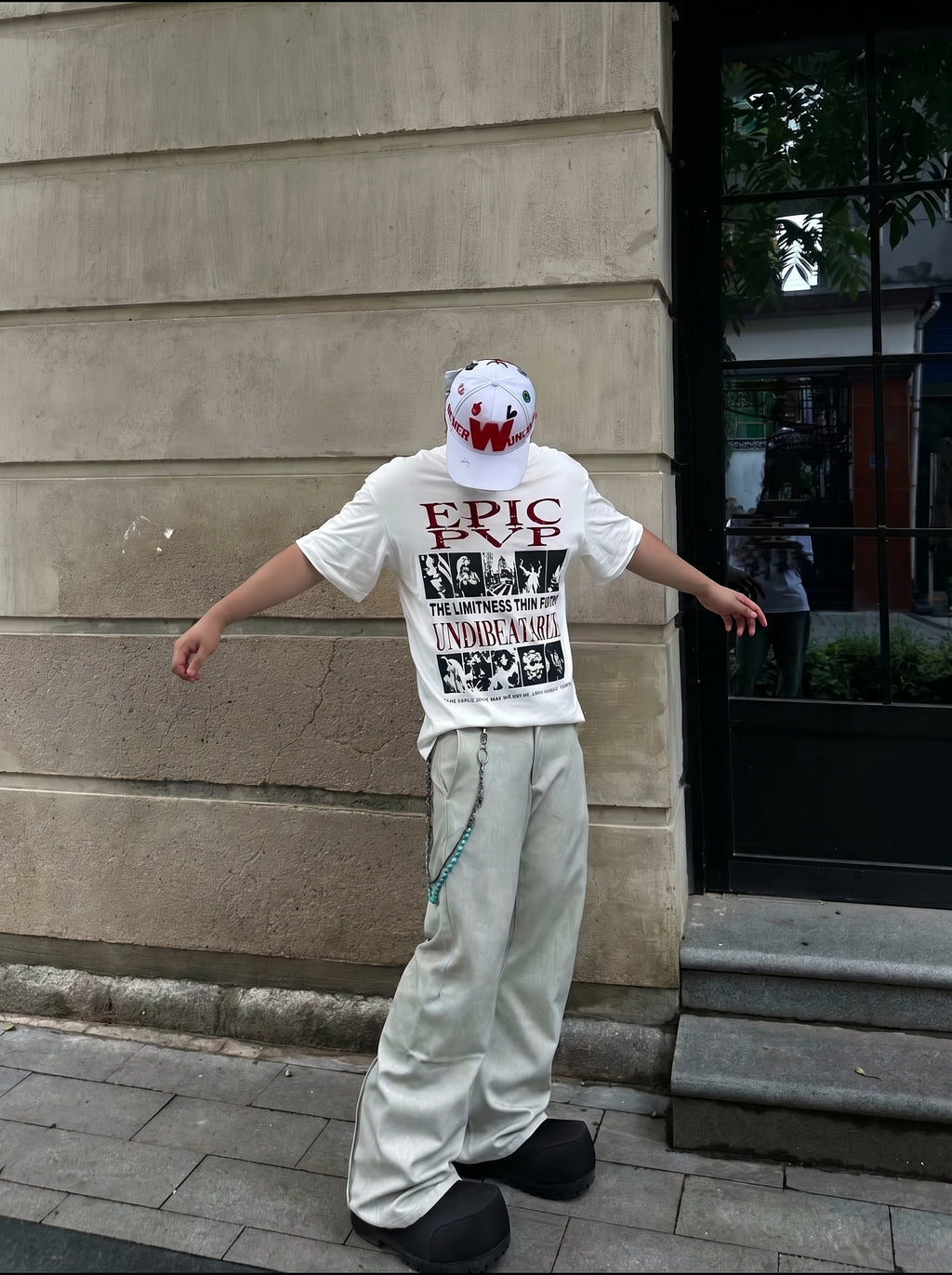 Person wearing a white t-shirt with text and graphics, standing against a building wall.