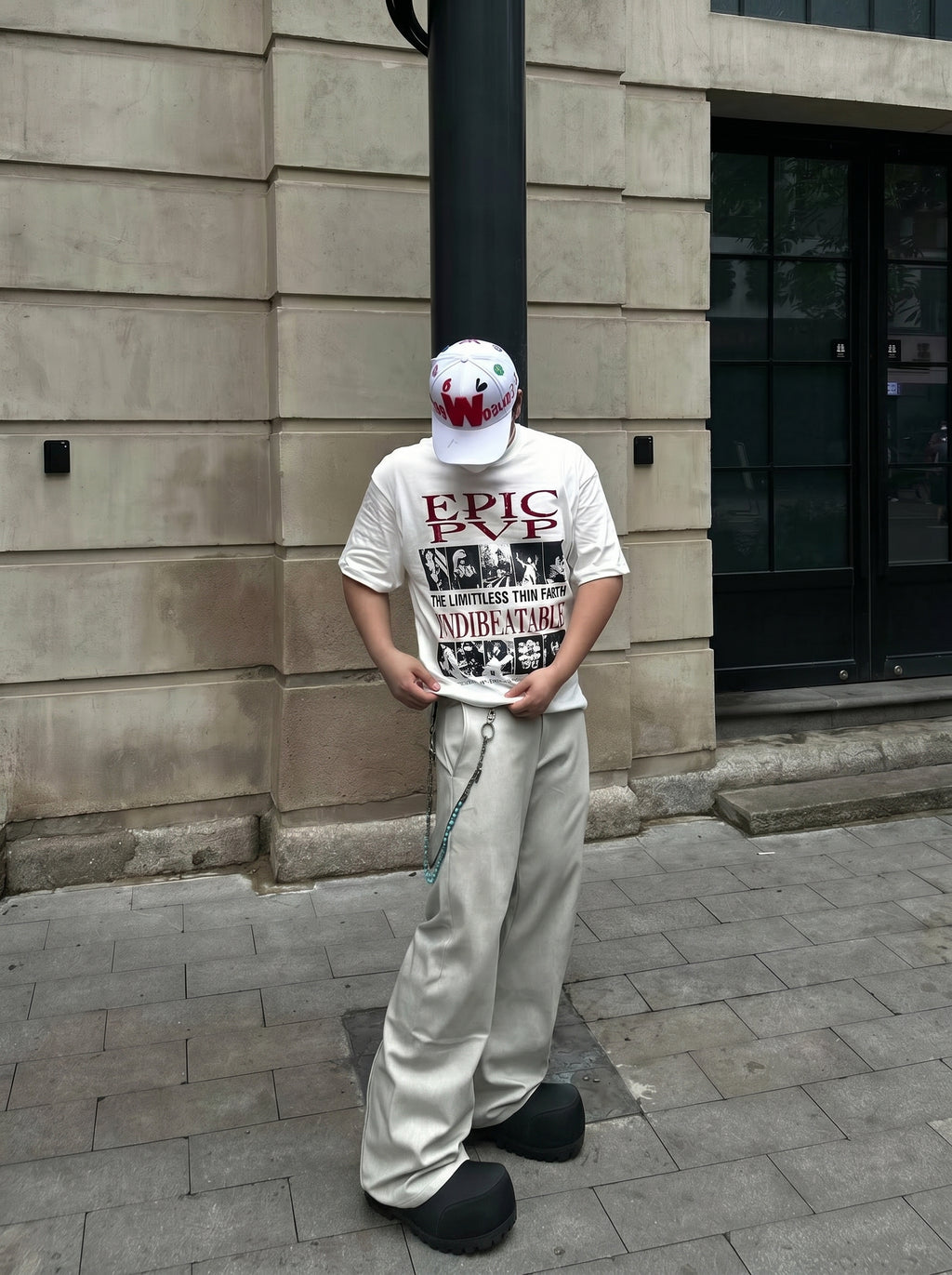 Person wearing a white t-shirt with text and a graphic, standing against a building wall.